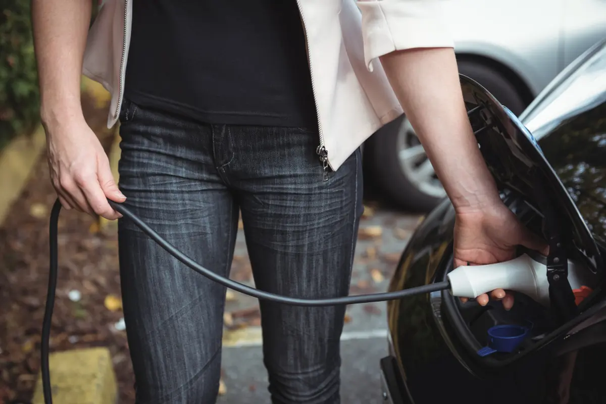 Ragazzo con in mano un cavo di ricarica elettrica mentre fa rifornimento